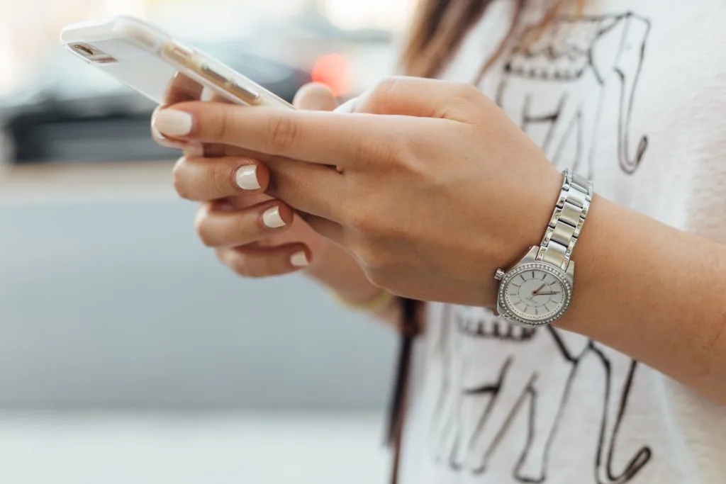 femme tenant un smartphone blanc avec montre argentée au poignet