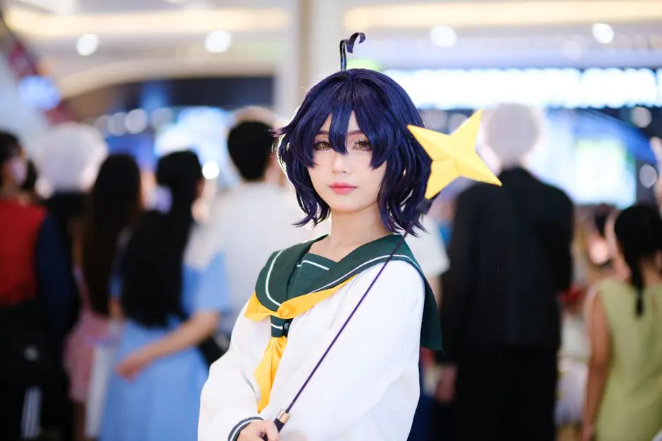 Cosplayer dressed as anime character with a star wand at a bustling indoor event.