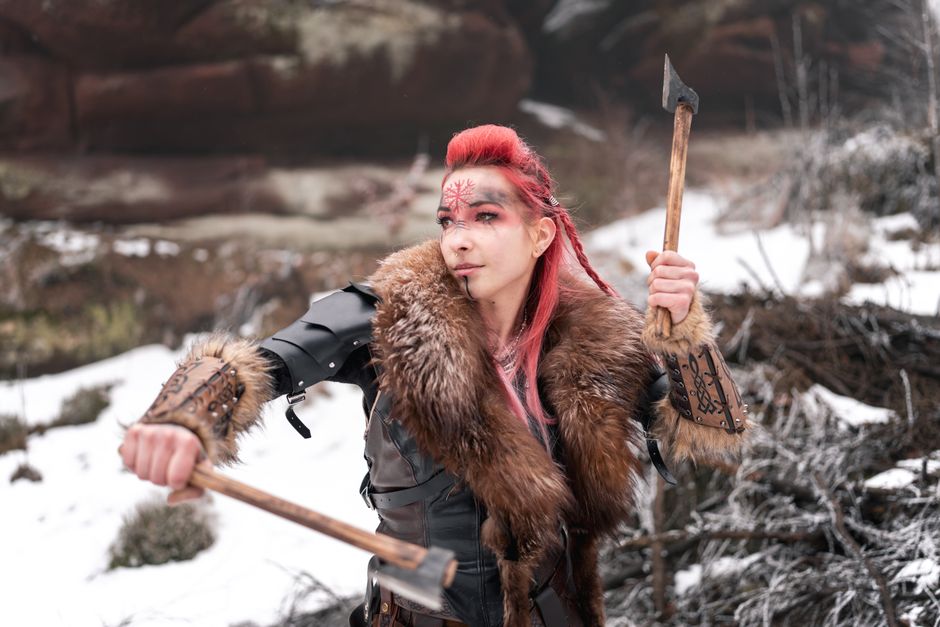 Viking woman in winter armor holding axes, ready for battle; fierce and determined.