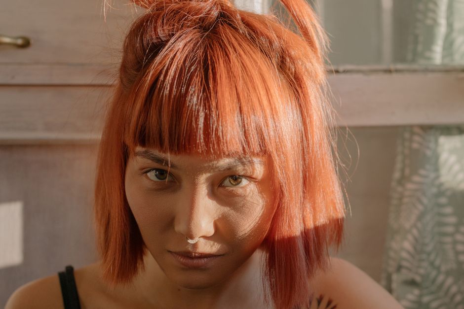 Close-up portrait of a woman with vibrant red hair illuminated by natural sunlight. Indoors setting.