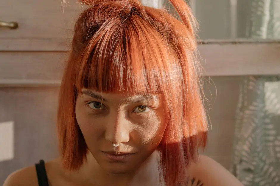 Close-up portrait of a woman with vibrant red hair illuminated by natural sunlight. Indoors setting.